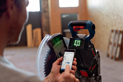 Person använder en smartphone för att kontrollera en digital skärmaskin med en synlig display inomhus.