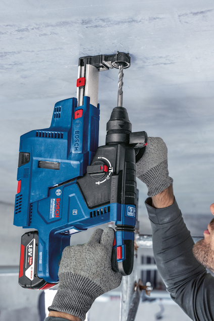 En person borrar i ett tak med en blå Bosch borrmaskin, och bär gråa arbetshandskar.