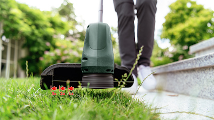 Grästrimmer i användning nära stentrappa, grön gräsmatta i förgrunden.