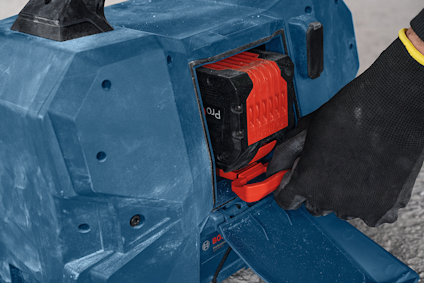 Batteripaket sätts in i ett verktyg av blå plast. En hand med svart handske hanterar batteriet.