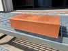 Röd tegelsten ligger på en metallhylla utomhus i solljus.