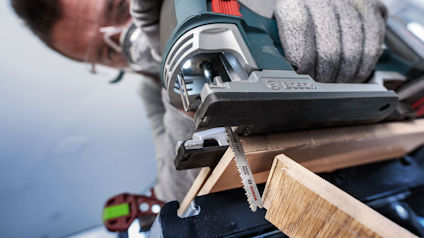 Person använder en elektrisk sticksåg för att såga en träbit.