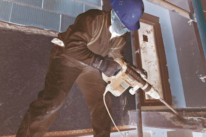 Arbetare i vit overall och gul hjälm använder en borrmaskin på en byggarbetsplats.