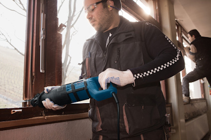 Person använder en elektrisk såg för att skära i fönster. Ytterligare person arbetar i bakgrunden.