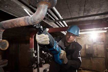 Person med blå hjälm använder en eldriven såg för att kapa ett rör i en industrimiljö.
