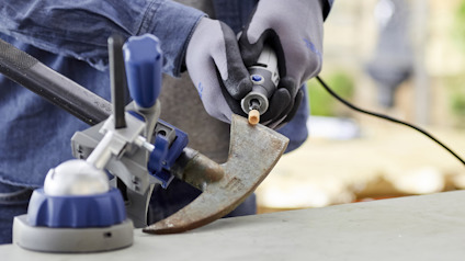 Person slipar en rostig yxa med en eldriven slipskiva och håller yxan i ett skruvstäd.