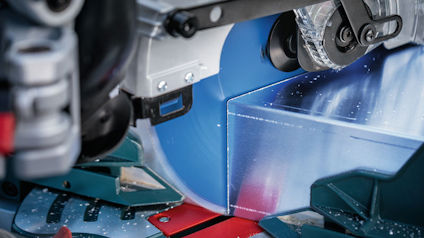 Närbild av en kapmaskin i arbete, med ett roterande blått sågblad och metallspån.