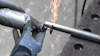 Person med arbetsvantar använder ett Dremel-verktyg för att kapa ett metallrör, gnistor flyger.