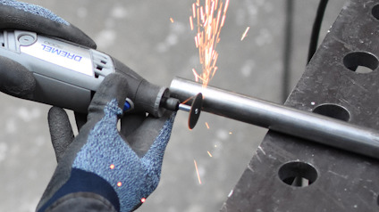 Person med arbetsvantar använder ett Dremel-verktyg för att kapa ett metallrör, gnistor flyger.