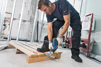 En person med skyddsglasögon och hörselskydd använder en elektrisk såg för att kapa trä på en byggarbetsplats.