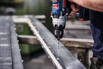 Person använder borrmaskin för att göra hål i metallbalk.