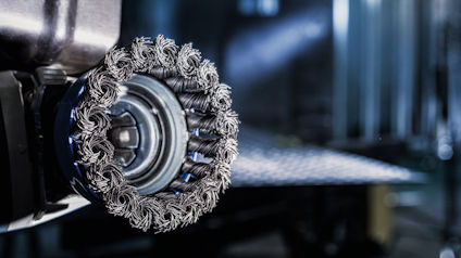 Rund stålborste fäst vid en maskin, med sammanflätade borst. Bakgrunden är suddig och industriell.