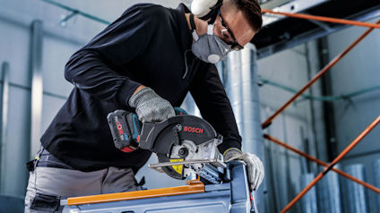Person sågar med en Bosch cirkelsåg, iförd skyddsglasögon och ansiktsmask.