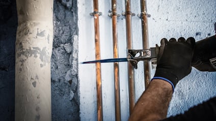 Hantverkare applicerar isolerande skum runt kopparrör som är monterade på en betongvägg.