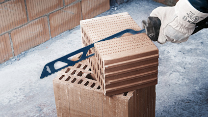 Hand med handske som håller en blå verktyg över staplade tegelblock.