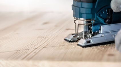 Sticksåg skär genom en träplanka, sågspån synliga på ytan.