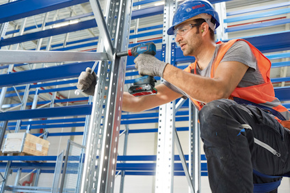 Person i skyddshjälm och väst använder en skruvdragare för att montera metallställningar.