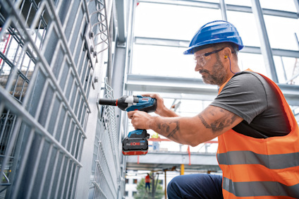 En person med skyddsutrustning använder en skruvdragare på en metallstruktur.
