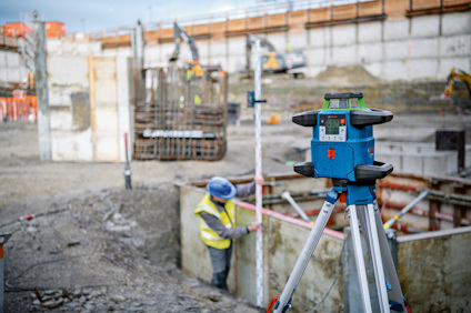 Byggarbetsplats med laserinstrument på stativ och arbetare i bakgrunden.