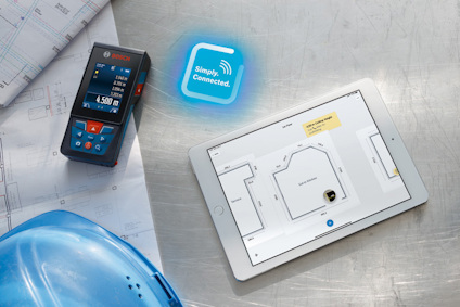 Tablet på bord med byggplan, digital avståndsmätare och blå hjälm. Tablet visar planritning och text: "Simply. Connected."