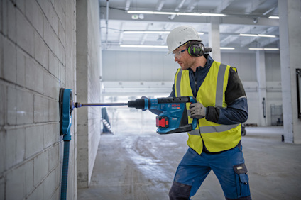 Person i reflexväst och hjälm använder borrmaskin på betongvägg.