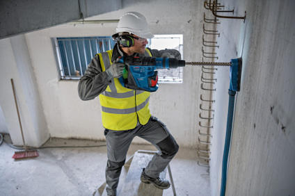 Byggnadsarbetare i reflexväst borrar i en betongvägg med borrarutrustning.