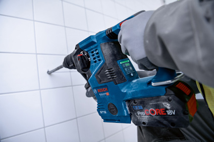 En person håller en blå handhållen borrmaskin från Bosch, ProCore 18V, mot en kaklad vägg.