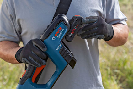 Person i grå tröja och svarta handskar håller i ett blått verktyg och lägger i ett batteri.