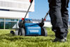 Person klipper gräset med en blå gräsklippare på en gräsmatta nära en modern byggnad.
