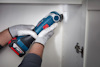 Person med handskar slipar insida av ett vitt skåp med en blå och röd sladdlös slipmaskin.