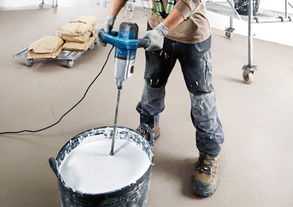 Person blandar vit färg eller gips i en hink med en elektrisk borr.