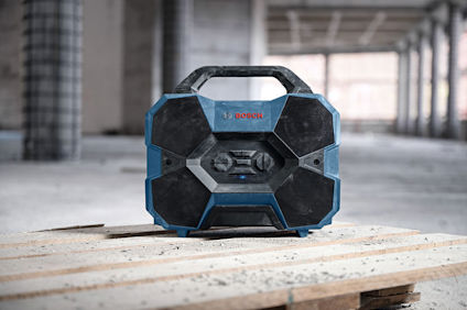 Bärbar högtalare från Bosch på byggarbetsplats, med dammig omgivning och utsikt över betongpelare.