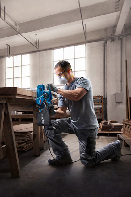 En person arbetar med en såg i en verkstad, iklädd skyddsglasögon och hörselskydd.