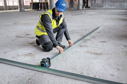 Person i byggutrustning använder en laseravståndsmätare för att mäta på en betongyta.