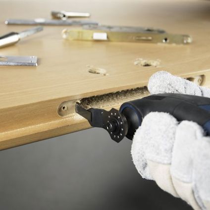 En person använder ett elverktyg för att borra i en träskiva, omgiven av metallverktyg.