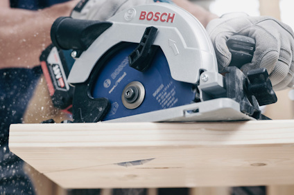 Cirkelsåg från Bosch skär genom trä; sågspån flyger. Handskar används för säkerhet.