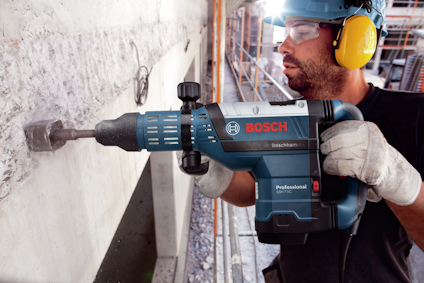 Man i skyddsutrustning använder blå Bosch borrmaskin mot betongvägg.