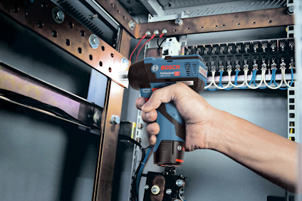 En hand håller en Bosch termometer inne i en teknisk panel med kablar och kopplingar.
