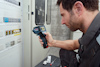 En person använder en Bosch infraröd termometer nära en elektrisk panel för att mäta temperatur.