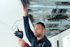 Man inspecting overhead pipes with a handheld device in a building interior.
