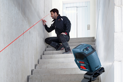 Man justerar röd lasernivå på trappa. Bosch verktyg på stativ.