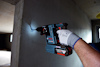 En person borrar i en betongvägg med en Bosch 18V borrmaskin, iklädd arbetshandskar och hjälm.