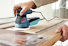 En person slipar en träyta med en Bosch excenterslipmaskin.