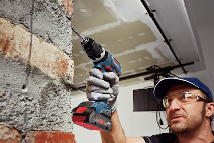 Person i byggkläder borrar i en betongvägg med en blå och svart borrmaskin.