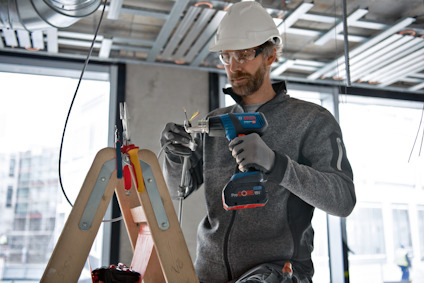 En person i byggmiljö använder en blå och röd batteridriven skruvdragare på ett projekt placerat på ett bockbord.