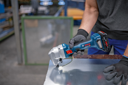 En person använder en sladdlös Bosch-metallsax på en metallplåt.