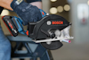 Hand som håller en svart och blå Bosch cirkelsåg. Saw-bladet är i rörelse. Bakgrund suddig.