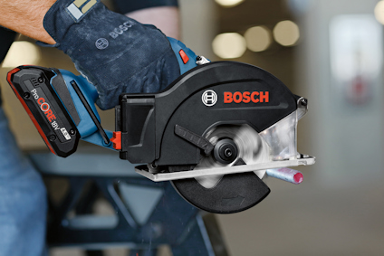 Hand som håller en svart och blå Bosch cirkelsåg. Saw-bladet är i rörelse. Bakgrund suddig.