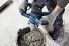 En person med handskar håller en elektrisk blandare som rör om cement i en hink.