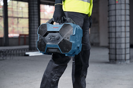 Person i arbetskläder håller en blå Bosch-verktygslåda i industriell miljö.